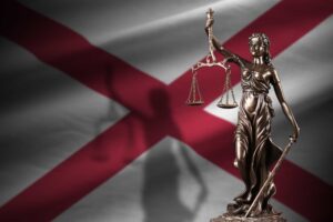Lady Justice statue holding scales of justice in front of Alabama state flag