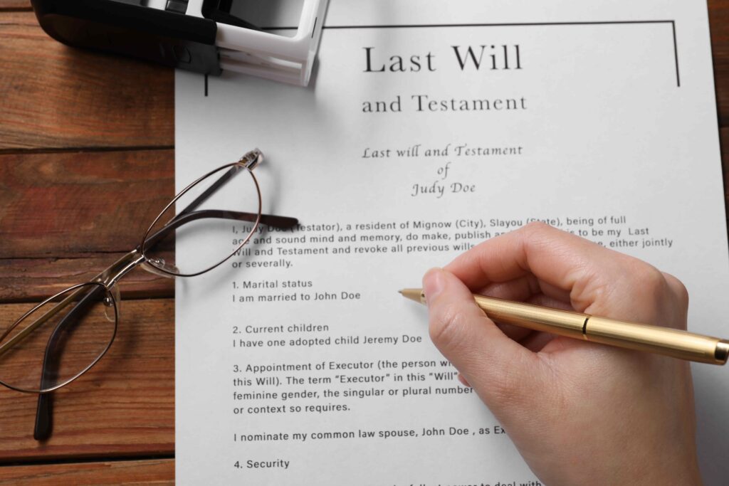 Last will and testament document being signed with glasses on wooden desk.
